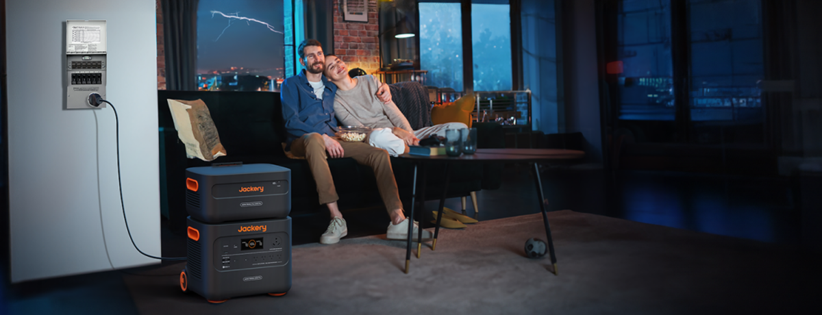 A couple sits on a couch in a dimly lit living room with ambient blue lighting. They're watching TV powered by the Jackery Explorer 2000 Plus Portable Power Station, featuring a LiFePO4 battery and ultra-fast solar charging capabilities.