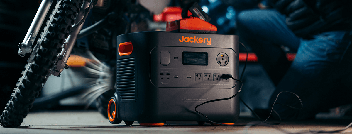 In the garage, a Jackery Explorer 3000 Pro Portable Power Station is positioned next to a motorcycle. It easily charges a gadget on top, showcasing its ultra-fast charging capabilities for quick device power-ups.