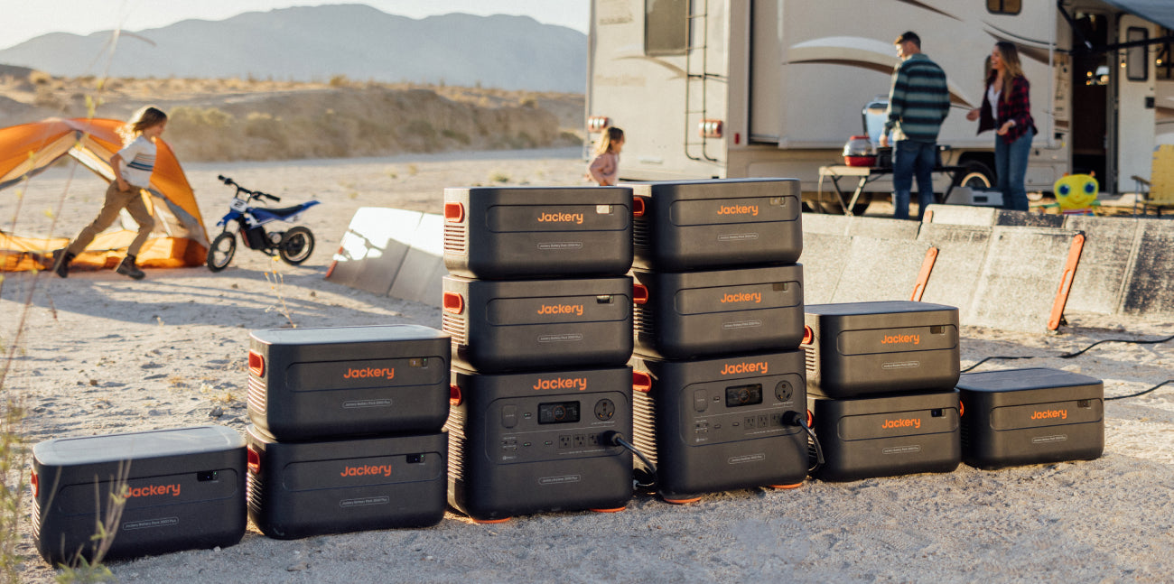 A Jackery Explorer 2000 Plus Portable Power Station with a LiFePO4 battery is shown outdoors in front of an RV. Nearby, a child plays by an orange tent and motorcycle, while two adults stand near the RV, all set against a desert landscape perfect for adventure and ultra-fast solar charging.