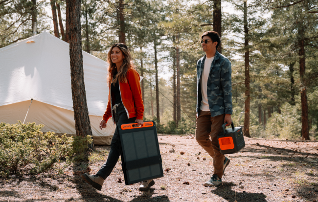 Two campers carrying a Jackery portable power station and folded solar panel